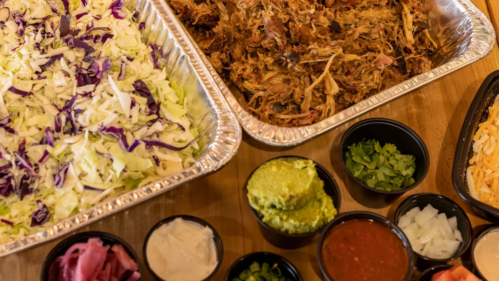 catering services, food from Breakfast Cantina restaurant in Sandpoint Idaho with two aluminum tins of shredded cabbage and lettuce shredded beef and a side of salsa, creme, guacamole, cheese, onions in Breakfast Cantina restaurant in Sandpoint Idaho