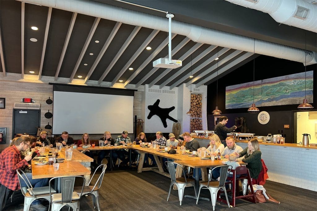 group of people eating at a rectangle u shaped wooden table with metal dining chairs for an event at Farmhouse Kitchen BBQ in Sandpoint, Idaho.