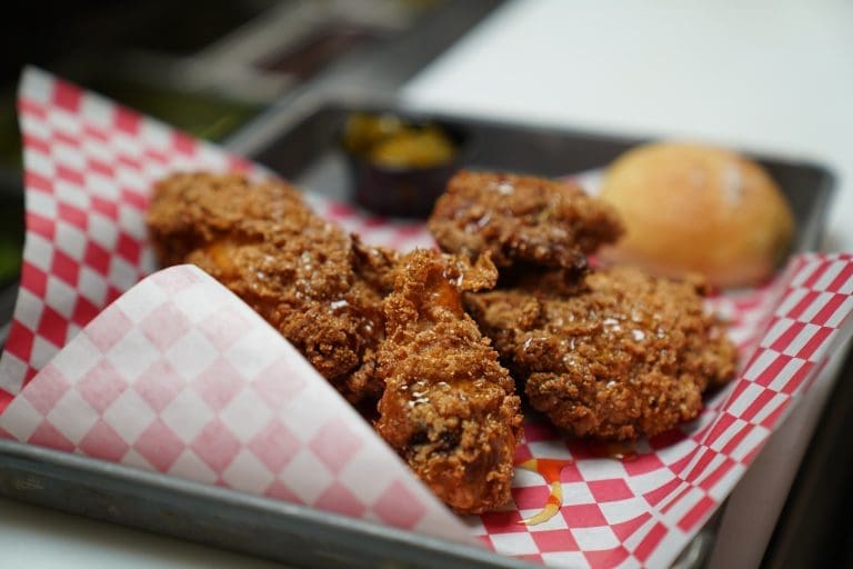 southern fried chicken from farmhouse kitchen bbq in sandpoint idaho with honey drizzle and a roll on the side on a red and white checkered pattern paper on a metal tray on a white counter